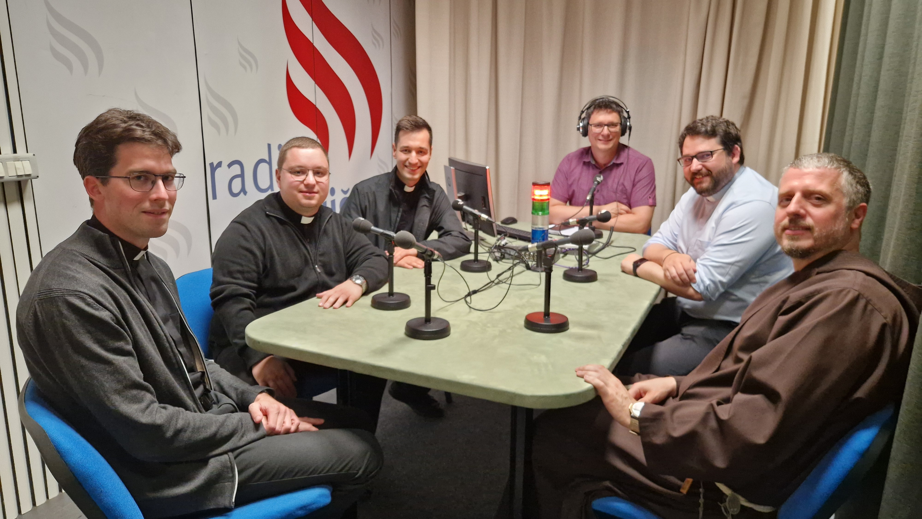 Luka Anžič, Timotej Fijavž Vivod, Gregor Anton Capucer, voditelj Matjaž Merljak, p. Janez Gorenc, br. Dominik Papež med snemanjem oddaje Naš gost